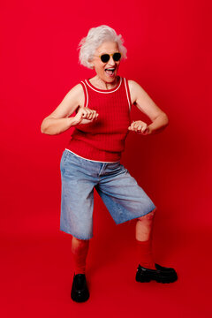 Energetic woman dancing in front of a red background wearing sunglasses and a red top