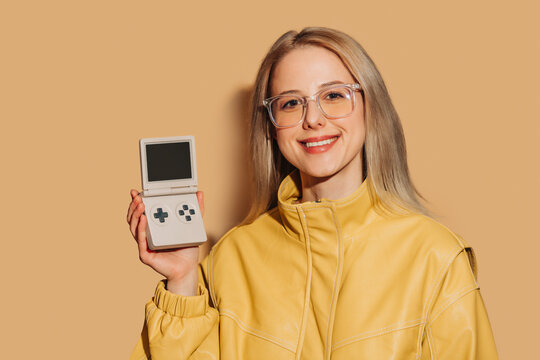 Smiling woman in yellow jacket holding a retro gaming console