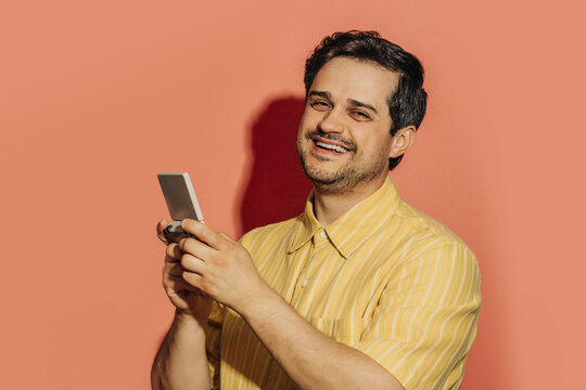 Smiling man in yellow shirt playing with a retro gaming console indoors