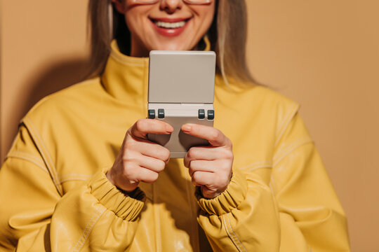 Smiling woman in yellow jacket playing with a retro gaming console indoors