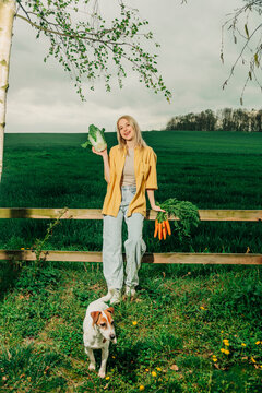 Woman holding vegetables with a dog in a rural green field