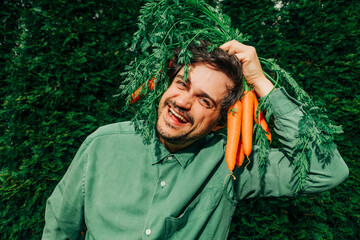 Man in green shirt holding carrots over his head and smiling outdoors