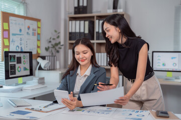Two Asian businesswomen discussing financial charts while using a calculator and tablet in a modern...