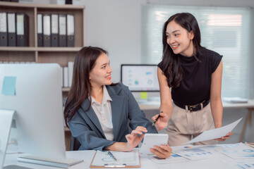 Two asian businesswomen are discussing and working together using calculator and documents,...