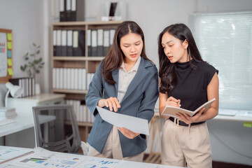 Two asian businesswomen are discussing financial report, pointing at charts and graphs, analyzing...