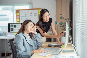Two asian businesswomen are discussing and analyzing financial data on a computer in a modern...