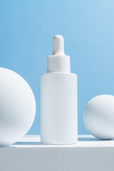 Facial serum in glass dropper bottle on white podium and balls on blue background. Natural skin care cosmetic. Beauty routine concept. Minimal composition. Trendy product for branding.