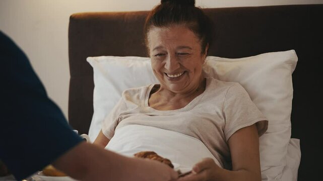 Retirement home worker bringing breakfast to elderly woman in bed, home care