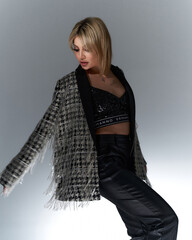 Blonde woman in modern fringe jacket and black leather pants, paired with a sequin top. She poses...