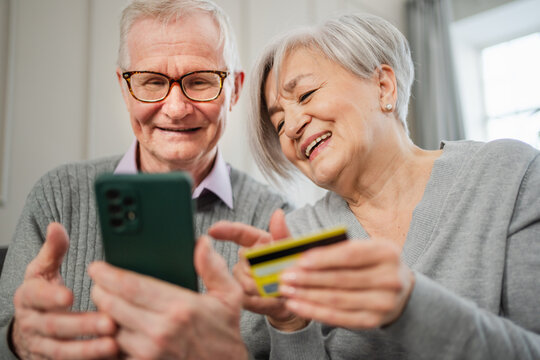 Senior couple man woman shopping online with smartphone paying with credit card. Old people buying on Internet enter credit card details at home indoors. Online shopping delivery service ecommerce - Powered by Adobe
