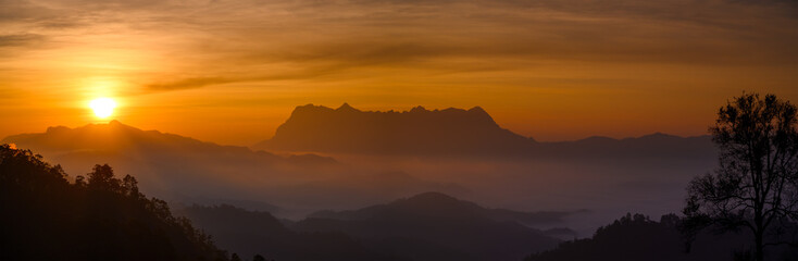 panoramic sunrise over Doi Chiang Dao with layers of misty mountains landscape and a golden orange sky, seen from Hadubi Camping