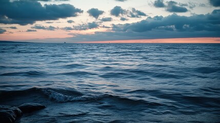 Obraz premium A tranquil ocean view at sunset with rippling waves and cloudy skies. Soft colors blend in the horizon, creating a calming atmosphere.