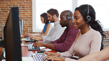 Multi-Cultural Business Team Wearing Headsets Working In Busy Customer Service Department