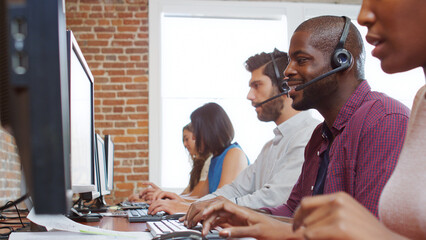 Multi-Cultural Business Team Wearing Headsets Working In Busy Customer Service Department