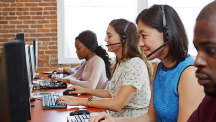 Multi-Cultural Business Team Wearing Headsets Working In Busy Customer Service Department