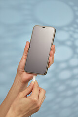 female hand plugging charger cord into smartphone to charge battery on blue background, Wired charging