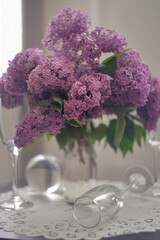 A delicate composition of blooming lilacs in a transparent jug and glass goblets.