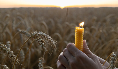 burning candle in female hands on wheat field at sunset. Conceptual photo in memory of Holodomor...