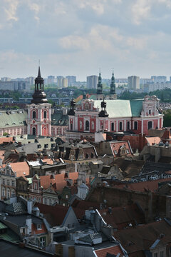 Poznan Basilica "Fara", a historic landmark with stunning architecture, rises amid city rooftops under a partly cloudy sky, blending past and present.
