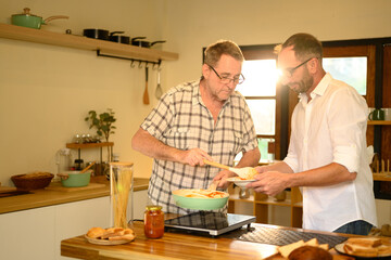 Cheerful mature father and adult son enjoy preparing a homemade meal together