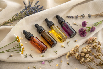 Aesthetic arrangement of essential oil bottles and dried flowers on a neutral fabric surface. Perfect for spa, wellness, and aromatherapy visuals.