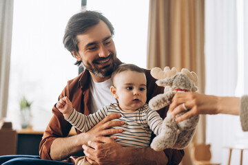 Happy father holding his baby son and playing with a plush toy