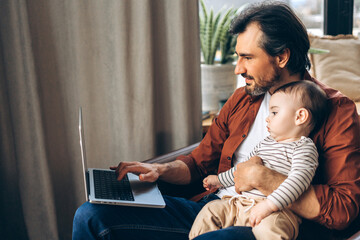 Father working from home and holding his baby son on his lap