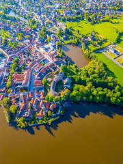 Fototapeta premium The charming town of Rozmital pod Tremsinem unfolds beside a peaceful river, showcasing historical architecture and vibrant greenery under clear skies, inviting exploration and discovery.
