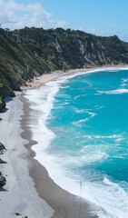 Scenic coastal landscape with dramatic cliffs and turquoise waves crashing onto a secluded sandy beach