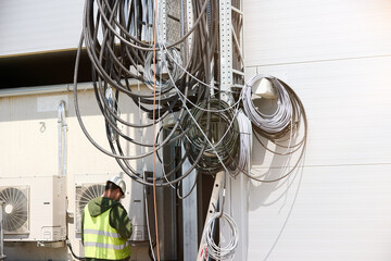 Electrician inspecting outdoor electrical wiring and HVAC units at industrial building. Ideal for: facility maintenance, energy infrastructure, HVAC installation, and electrical engineering.