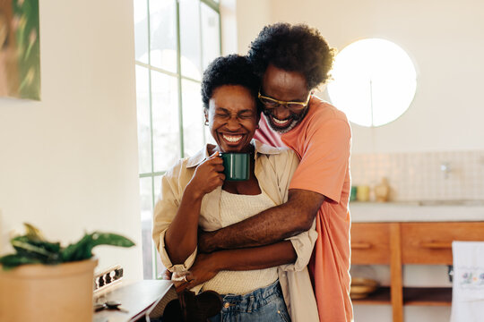 Mature man making his wife laugh in a tight hug at home
