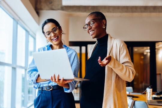 Two businesswomen discussing work while using a laptop in an office setting