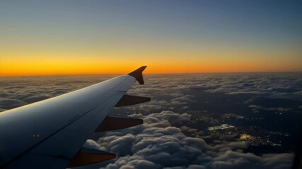 Aerial view of airplane wing over clouds at sunrise or sunset with city lights below - Powered by Adobe