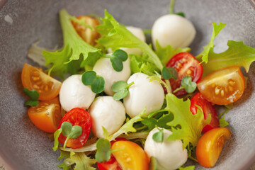Salad with lettuce, mozzarella and tomatoes in a plate on the table. Caprese salad.