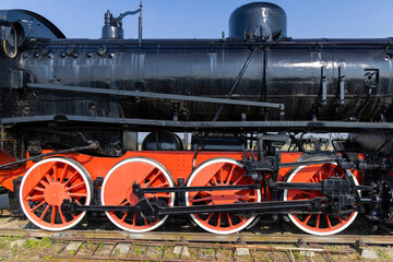 Naklejka premium Old black steam locomotive with red wheels standing on rails against blue sky