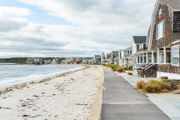 Empty paved footpath lined with tradtional wooden houses along a sandy beach on a cloudy autumn day