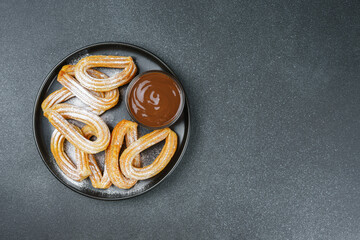 Traditional spanish dessert churros, fried dough pastry dusted with powdered sugar and chocolate sause on black background. Street food, sweet snack, homemade dessert. Top view, copy space