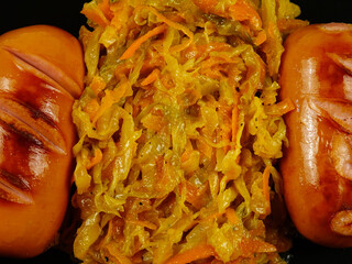 Stewed cabbage and grilled sausages are on a black plate, top view
