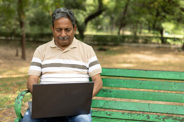 Indian senior man working on laptop in garden. Happy Elderly white-haired people smiling carefree,...
