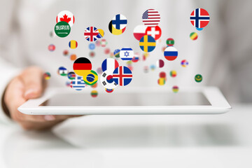 Image of various national flags hovering over a tablet, representing global communication and...