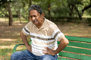 Indian painful senior man suddenly suffering stomach pain at park