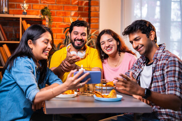 Watching funny clip while eating, Indian students laugh over chai and samosa in indoor cafe
