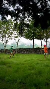 A young, cheerful guy catches a Frisbee and throws it back against the backdrop of trees, greenery, and a blue sky&mdash;on the Didina to Ali Bedni Bugyal trek in Uttarakhand, India.