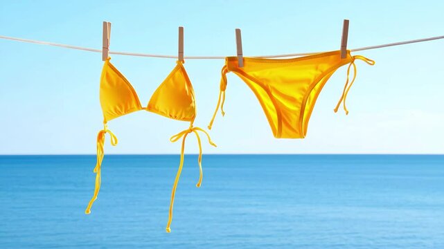 Yellow bikini swimsuit hanging on clothesline against blue sea and sky, beach vacation setting, summer swimwear drying outdoors, travel lifestyle background, sunny coastal mood