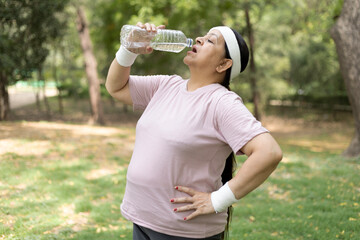 Indian overweight woman in sportswear drinking water after workout at park. Healthy lifestyle,...