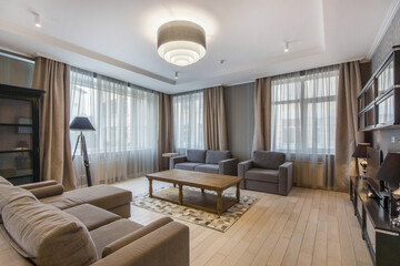 Elegant interior of the living room with large windows. The room is decorated in beige and gray tones. Elegant furniture.