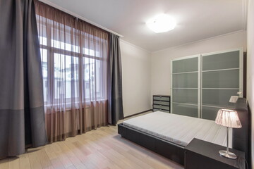 Bedroom interior with modern design. Dark furniture, wardrobe with frosted glass doors, window with beautiful curtains.