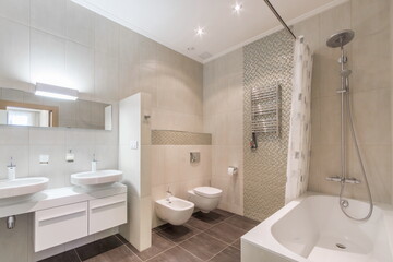 The interior of the bathroom, decorated in beige tones. Bath with shower, two sinks, electric heated towel rail.