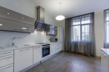 Magnificent kitchen interior with large windows. White kitchen set with built-in modern appliances....