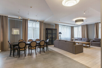 The interior of the living room with a beautiful design. Stylish furniture. Dining table with chairs, sofas and armchairs, windows with elegant curtains.
